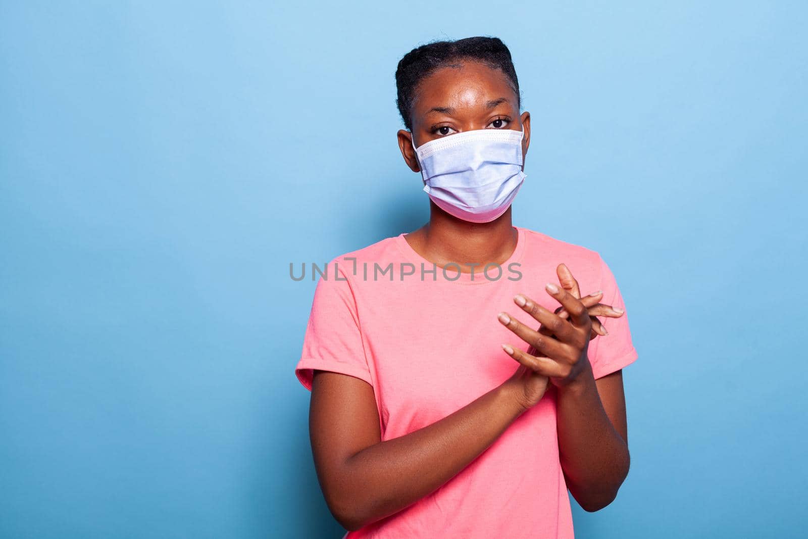 Portrait african american student with protection medical face mask to prevent infection with coronavirus clapping and applauding happy and joyful in studio with blue background. Victory concept