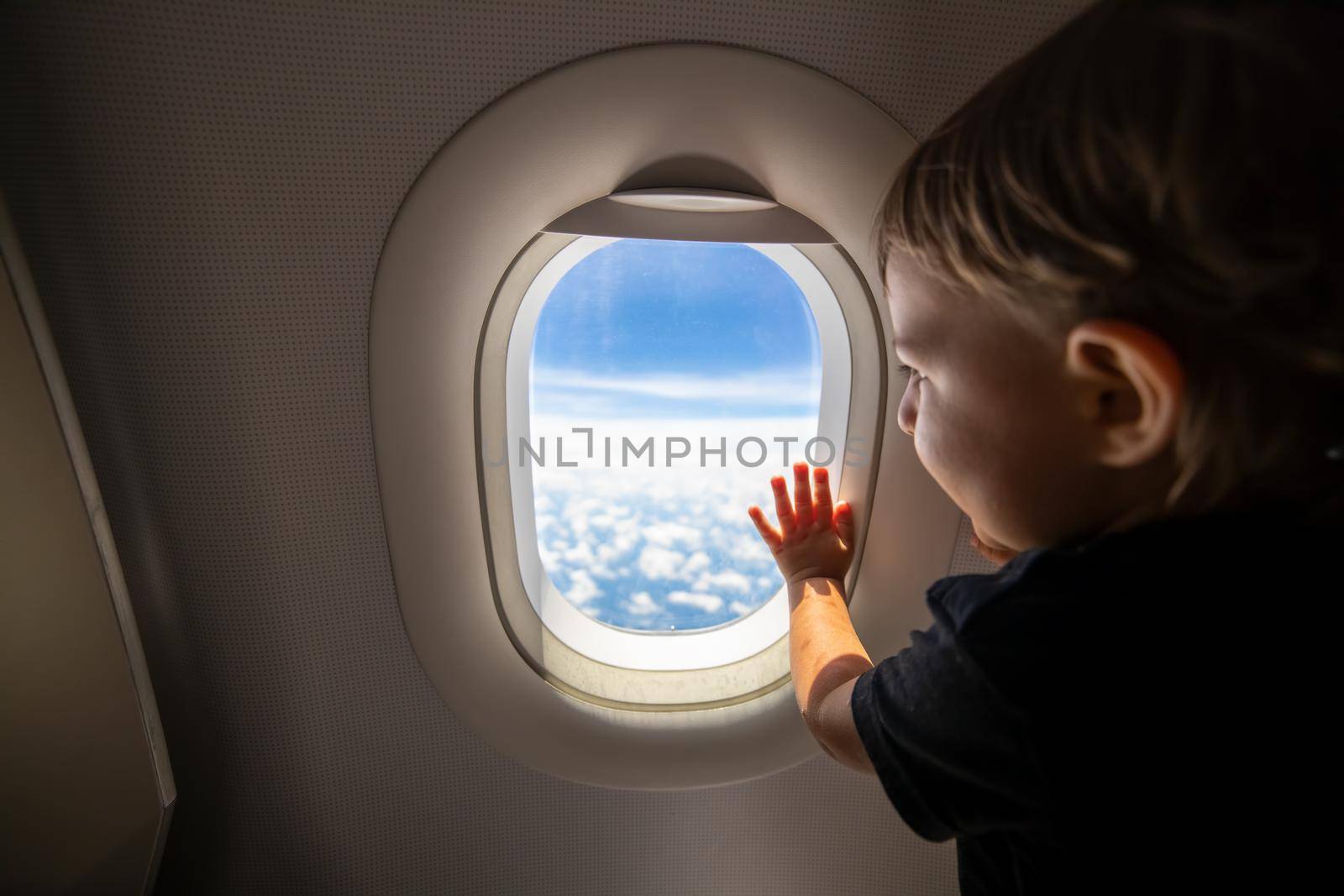 cute toddler points his finger at the sky through the window. first flight concept, traveling with children. by Mariaprovector