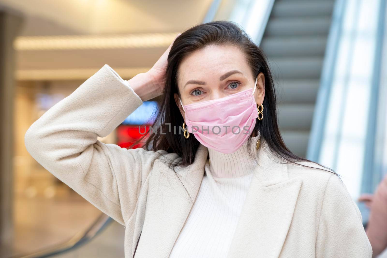 beautiful woman in a pink medical mask on her face against the background of the escadator in a public place.