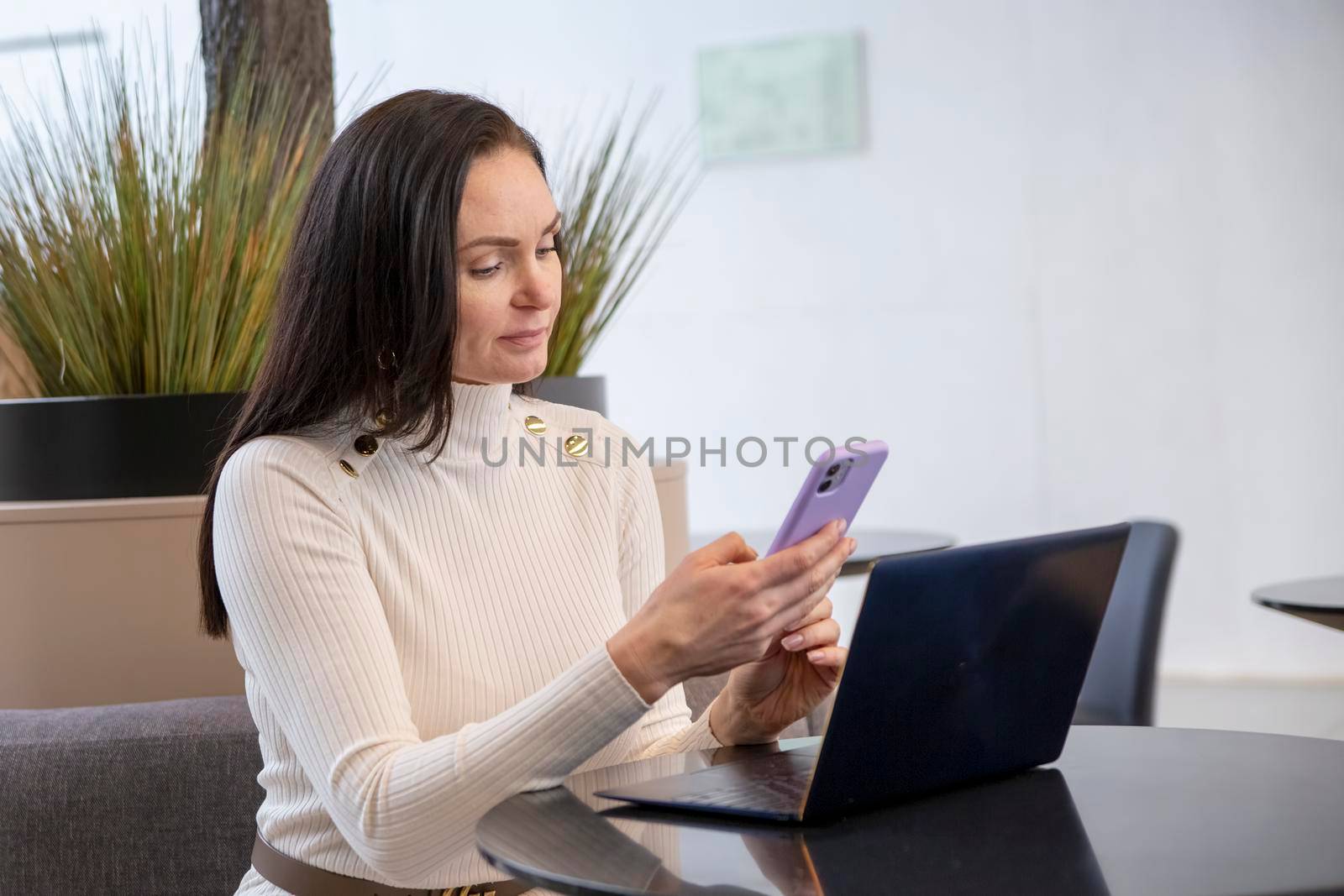 beautiful business woman typing on the phone while sitting at the table with laptop.
