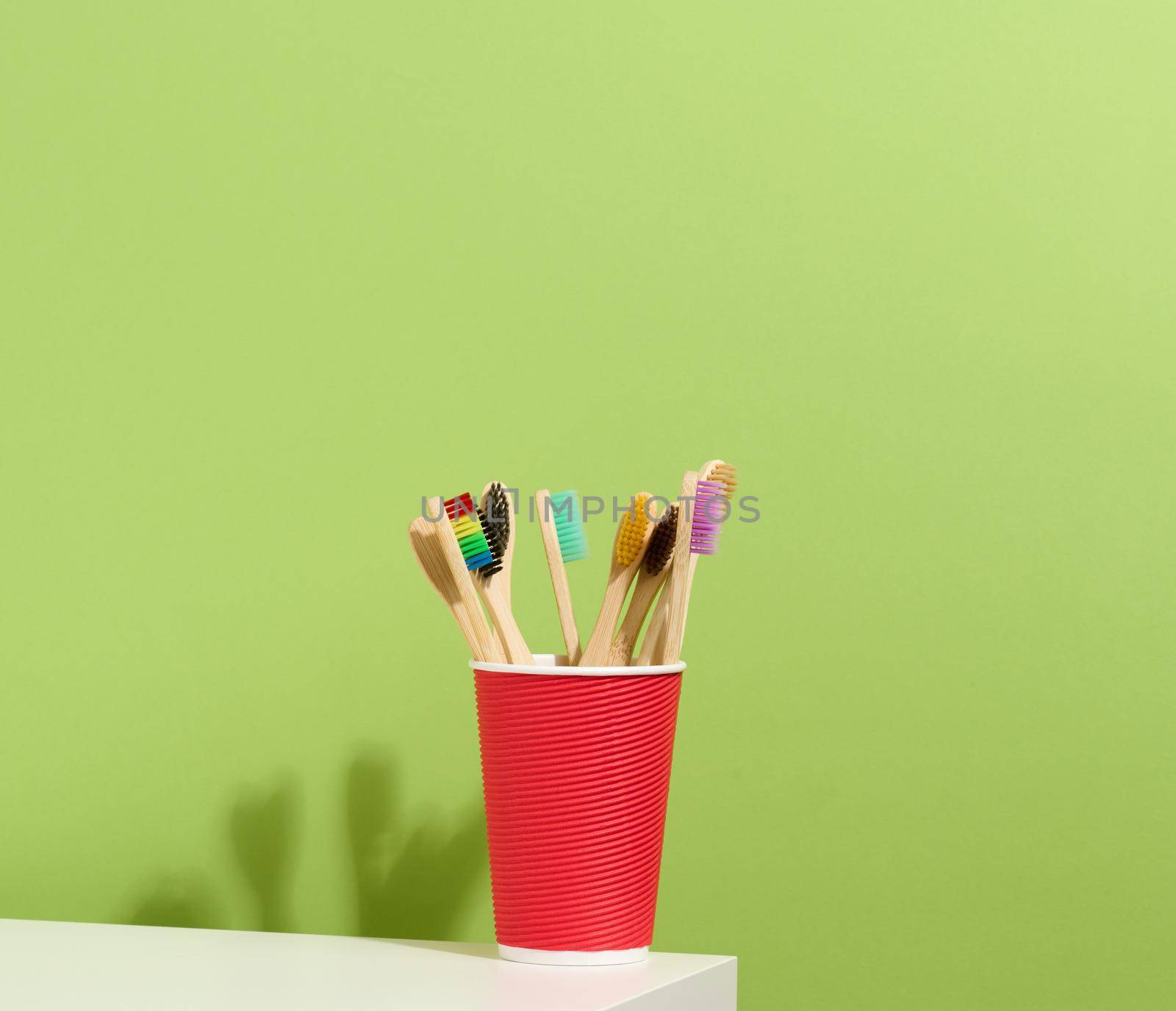 wooden toothbrushes in a paper cup on a white table. Green background, zero waste by ndanko