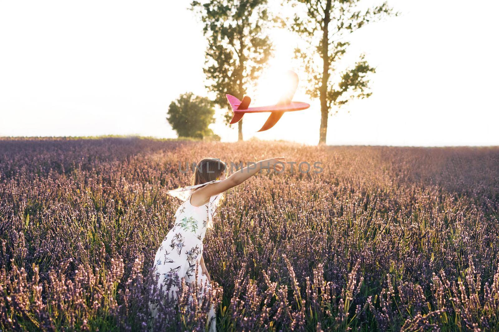 Little girl wants to become pilot and astronaut. Concept big child dream. Happy little girl playing with airplane on a lavender field during sunset. Children play toy airplane.