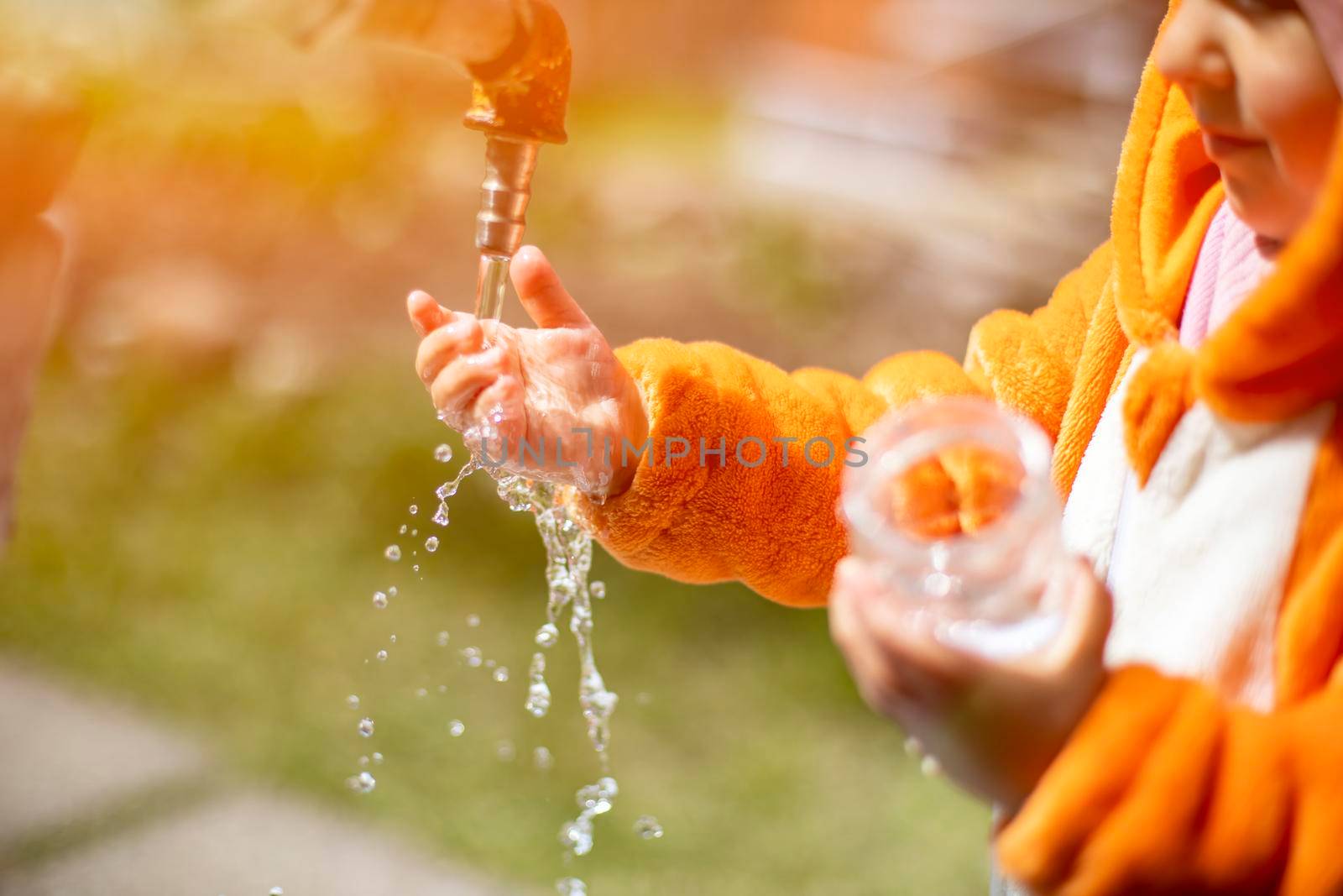 adorable toddler plays with water and tap in the sunshine