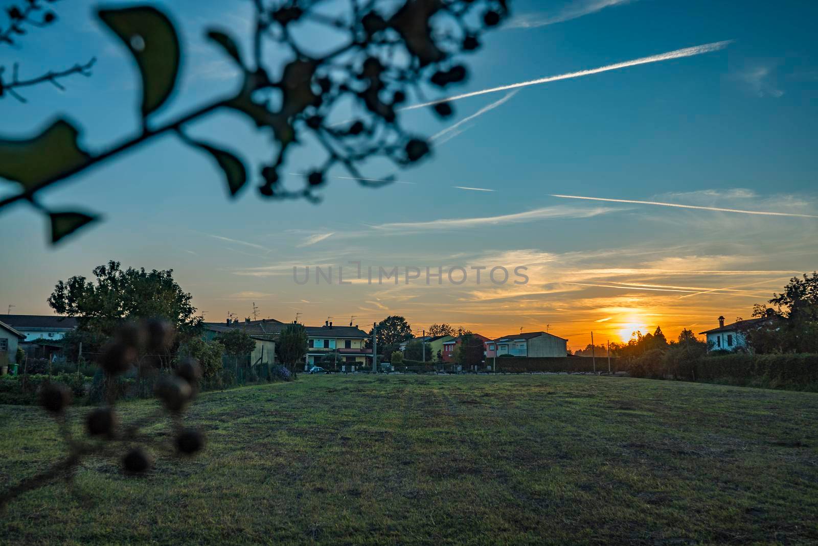 Rural landscape with beautiful gradient evening sky at sunset. Green field and village on horizon