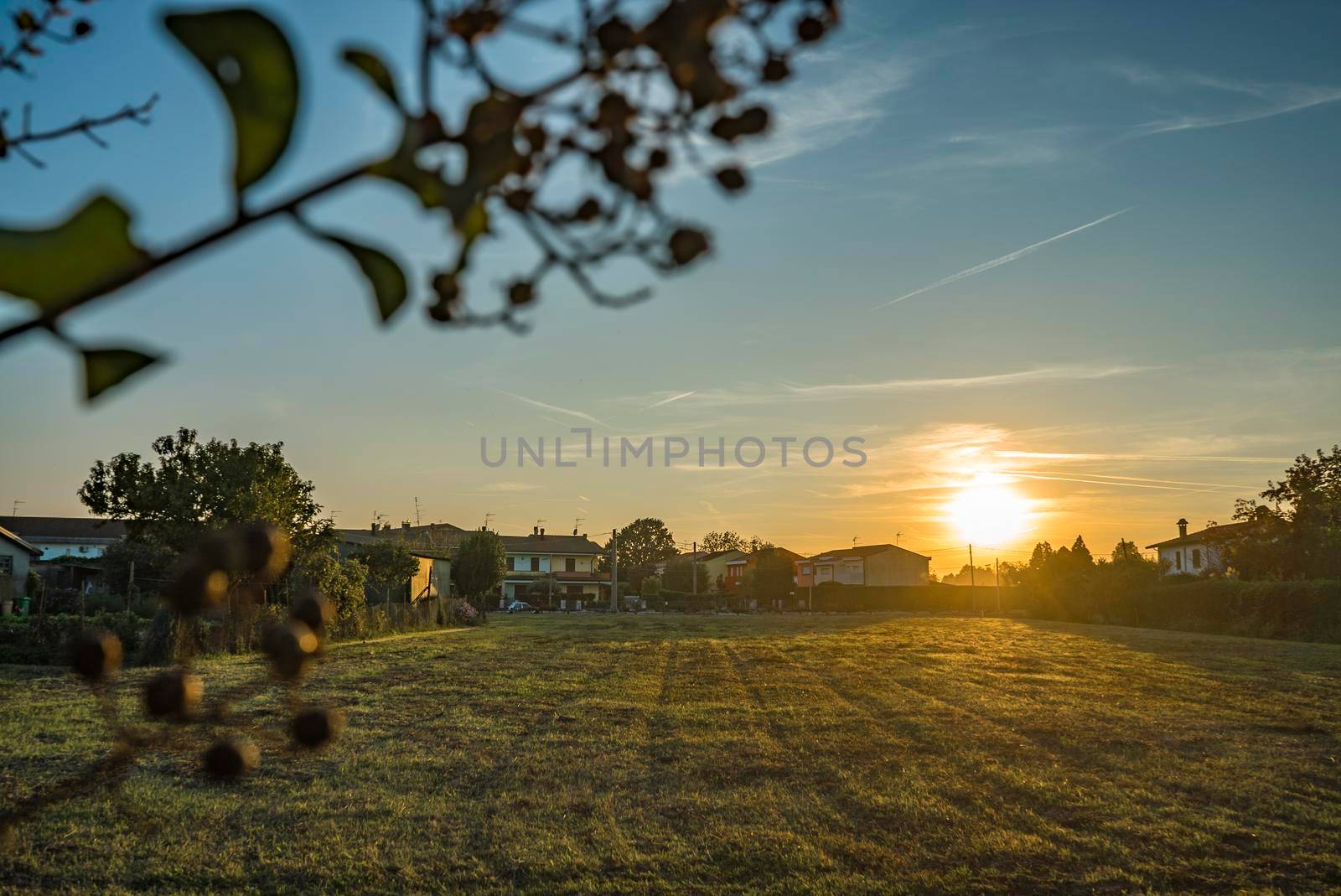 Rural landscape with beautiful gradient evening sky at sunset. Green field and village on horizon