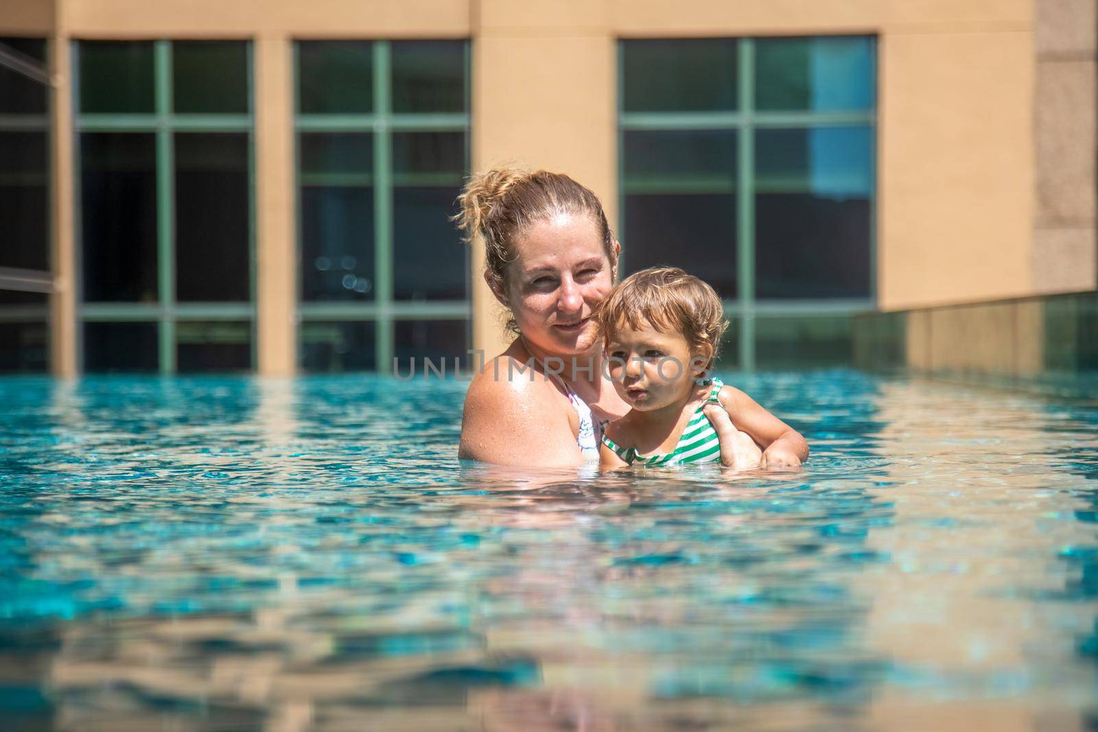 young mother rests her little toddler daughter in the city pool