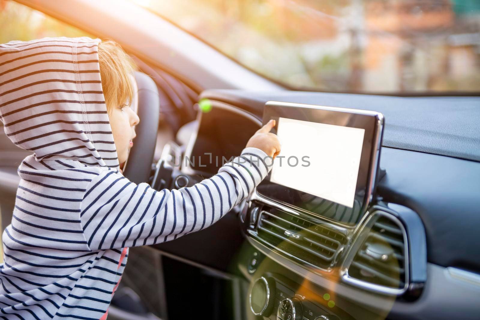 curious toddler girl holding, touching, and turning a car mnultiedia touch screen player button. empty white screen