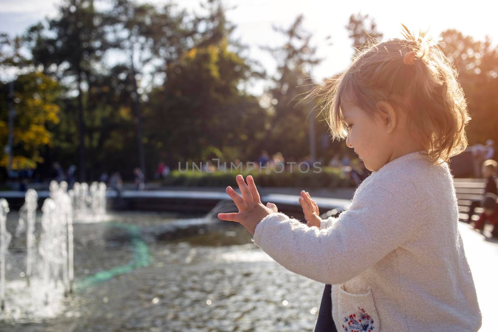 adorable toddler girl looks at the fountains in the park in the park on a sunny day.