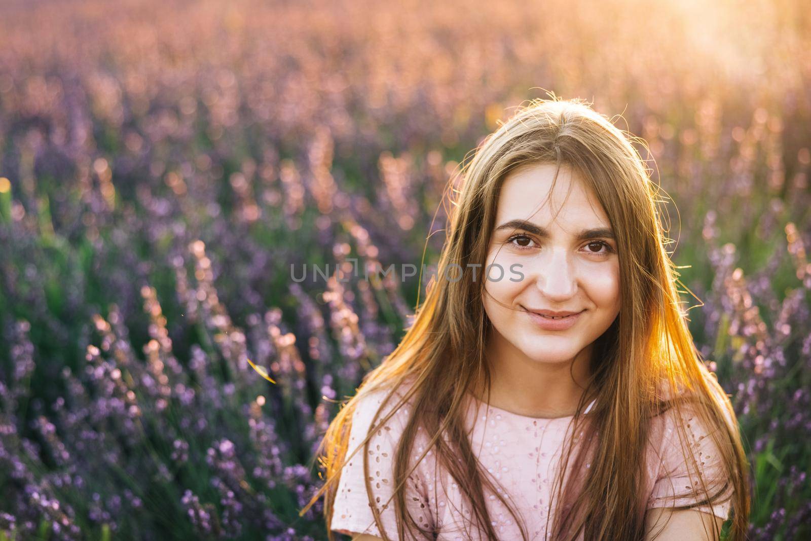 Beautiful woman is posing at field of purple lavender flowers. Beautiful woman in the lavender field on sunset in France .Girl collect lavender. Soft focus.