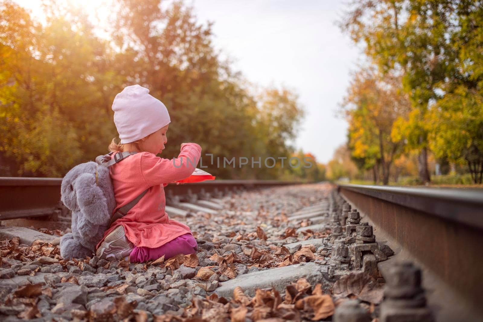 cute little toddler girl playing outdoors witch stone on the abandoned railway tracks.