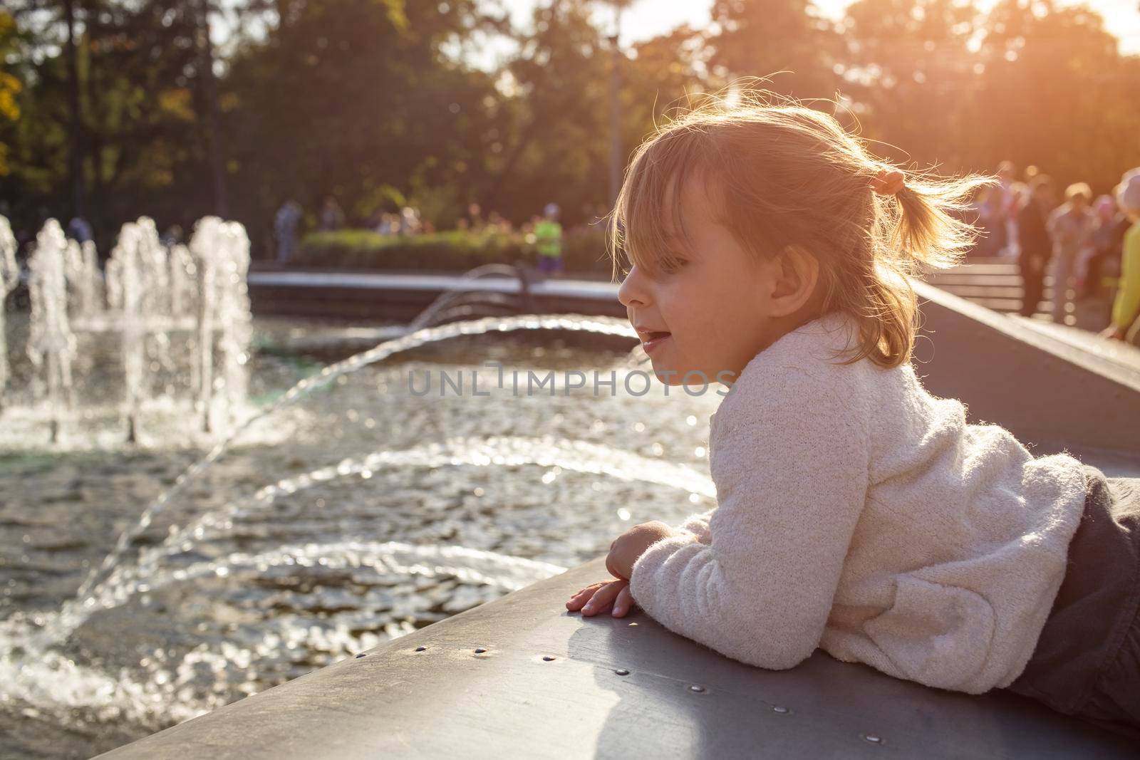 adorable toddler girl looks at the fountains in the park in the park on a sunny day by Mariaprovector