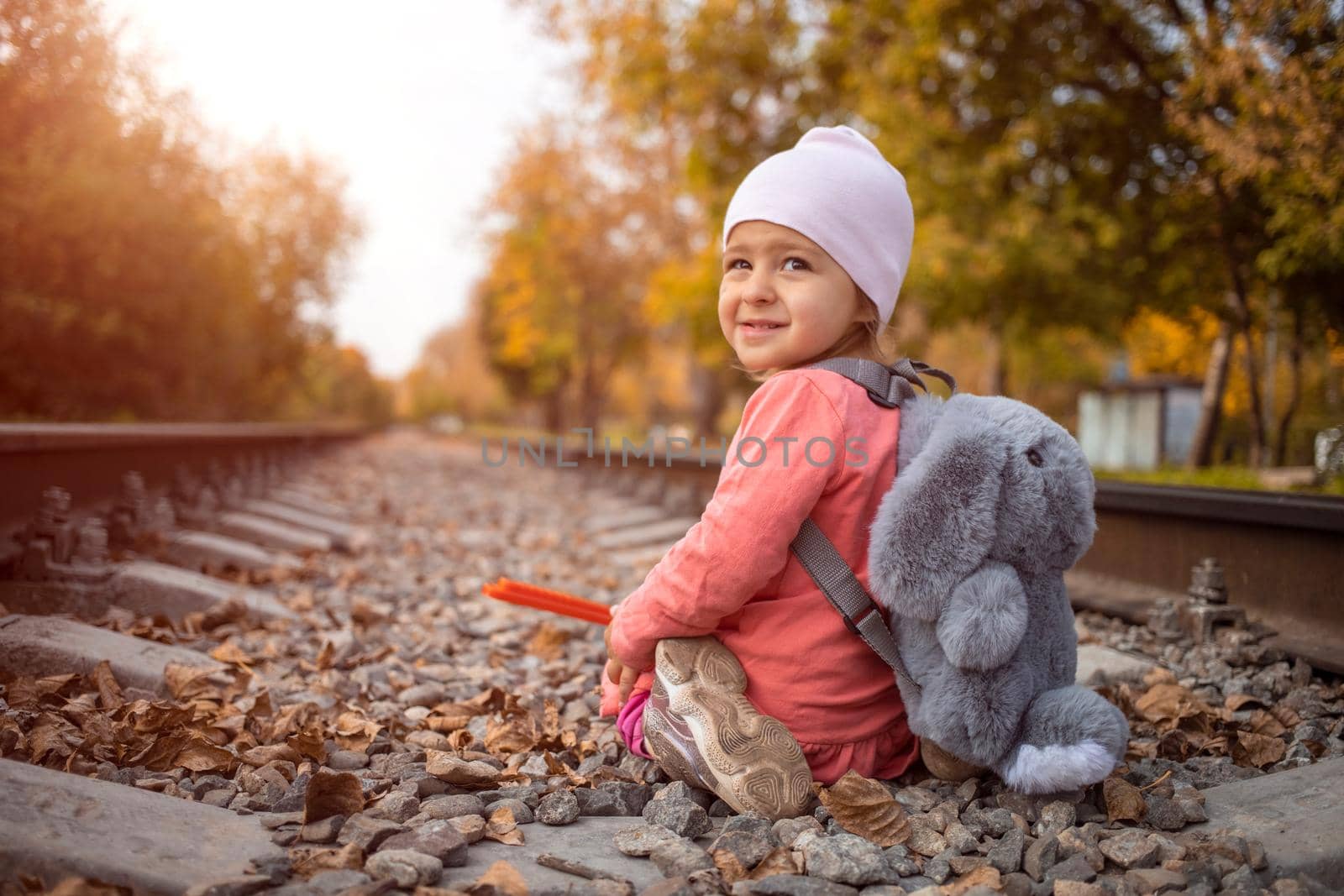children in danger concept. a cheerful girl sits on the railroad tracks and smiles slyly on sunny autumn day.