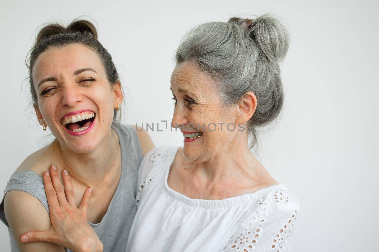 Happy senior mother is hugging her adult daughter, the women are laughing together, sincere family of different age generations having fun on white background, mothers day