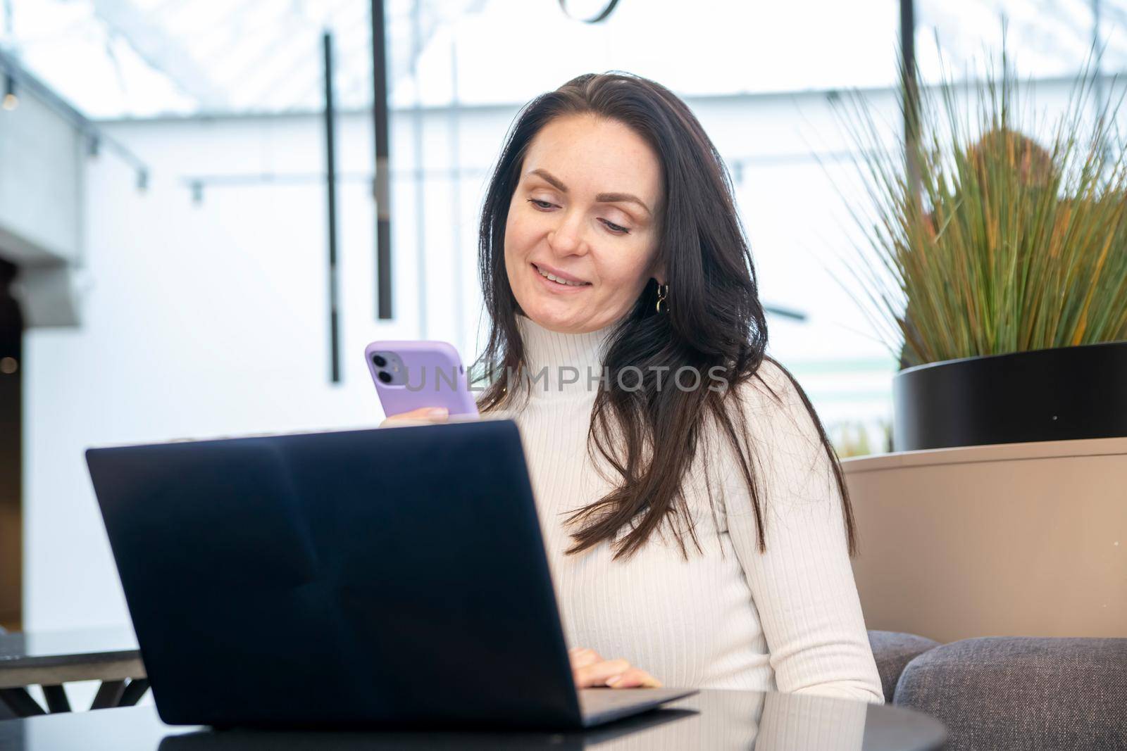 young woman works on laptop and smartphone in cafe.