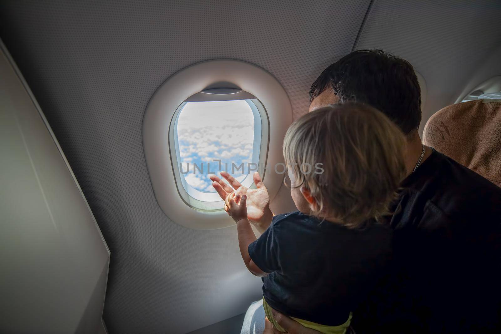 father and cute Toddler sitting on an airplane and looking at the sky through the porthole. first flight concept, traveling with children