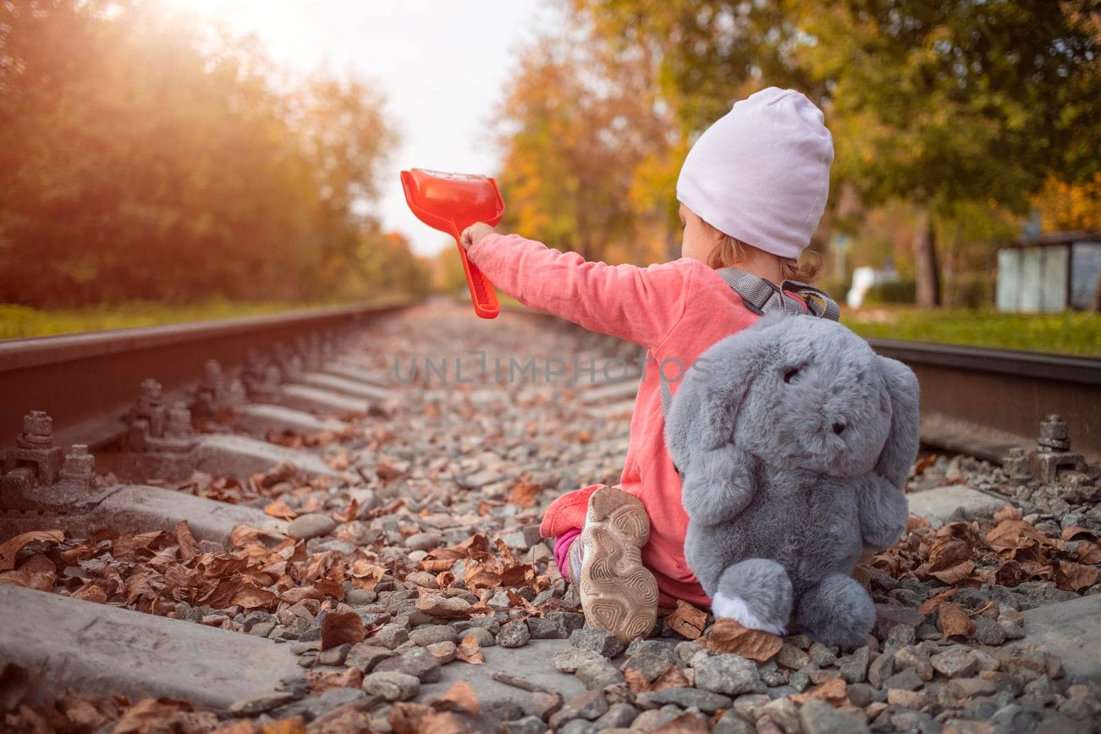 Caucasian girl with toy on railroad tracks on the sunny autumn day