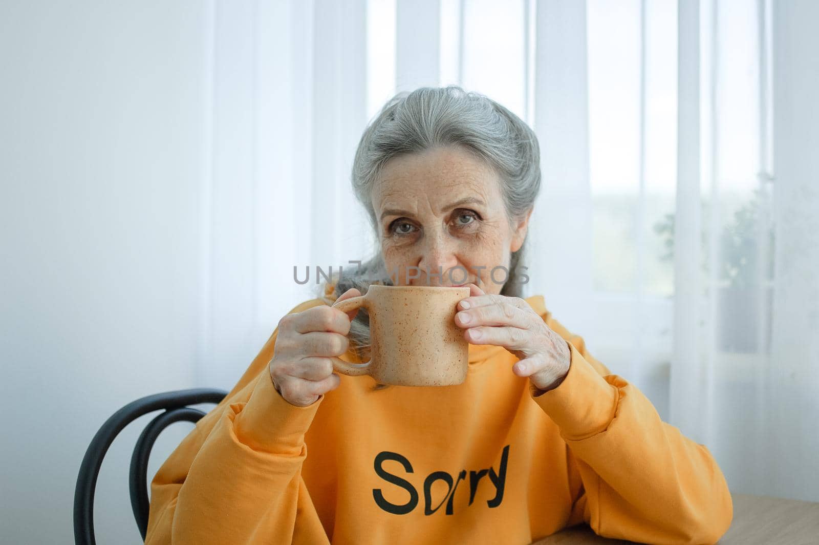 Elderly gray-haired woman is drinking coffee while sitting at home. Happy retirement.