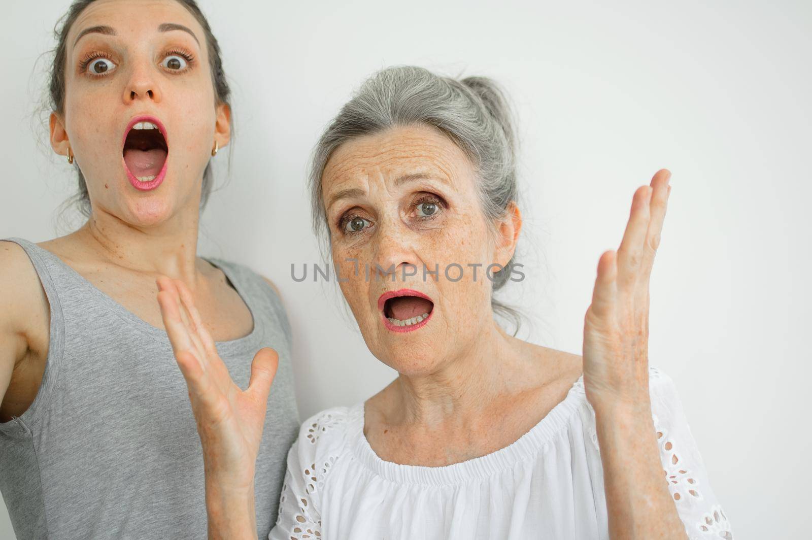 Emotional adult daughter with her senior moter are screaming and looking at the camera, crazy family of different age generations having fun on white background, mothers day.