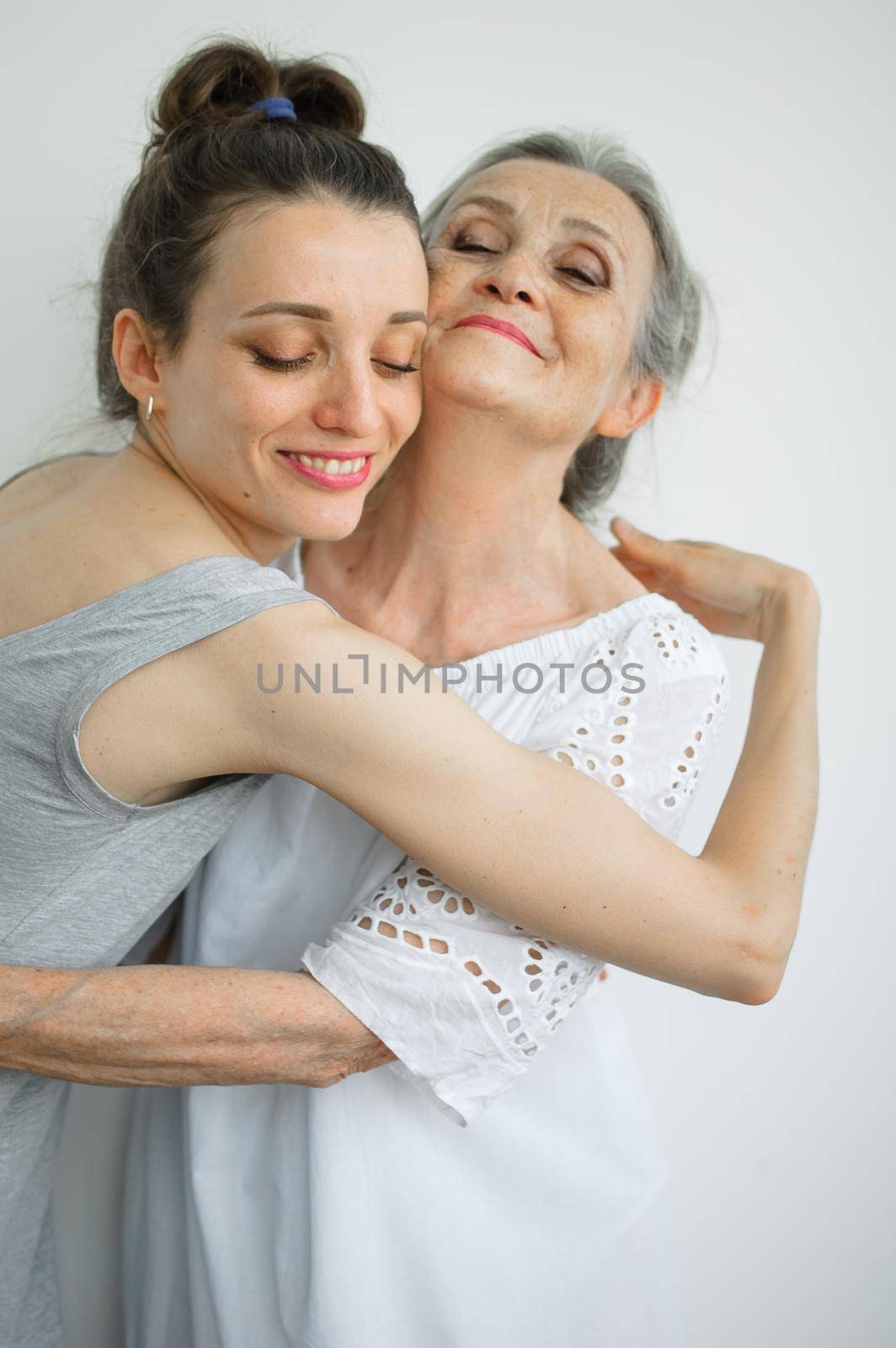 Happy senior mother is hugging her adult daughter, the women are laughing together, sincere family of different age generations having fun on white background, mothers day. by balinska_lv