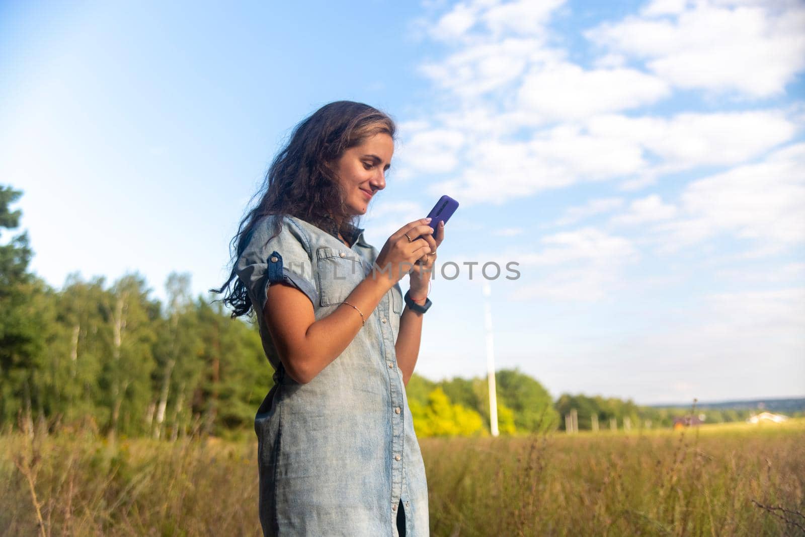 happy young woman looks into smartphone on nature background on sunny day by Mariaprovector