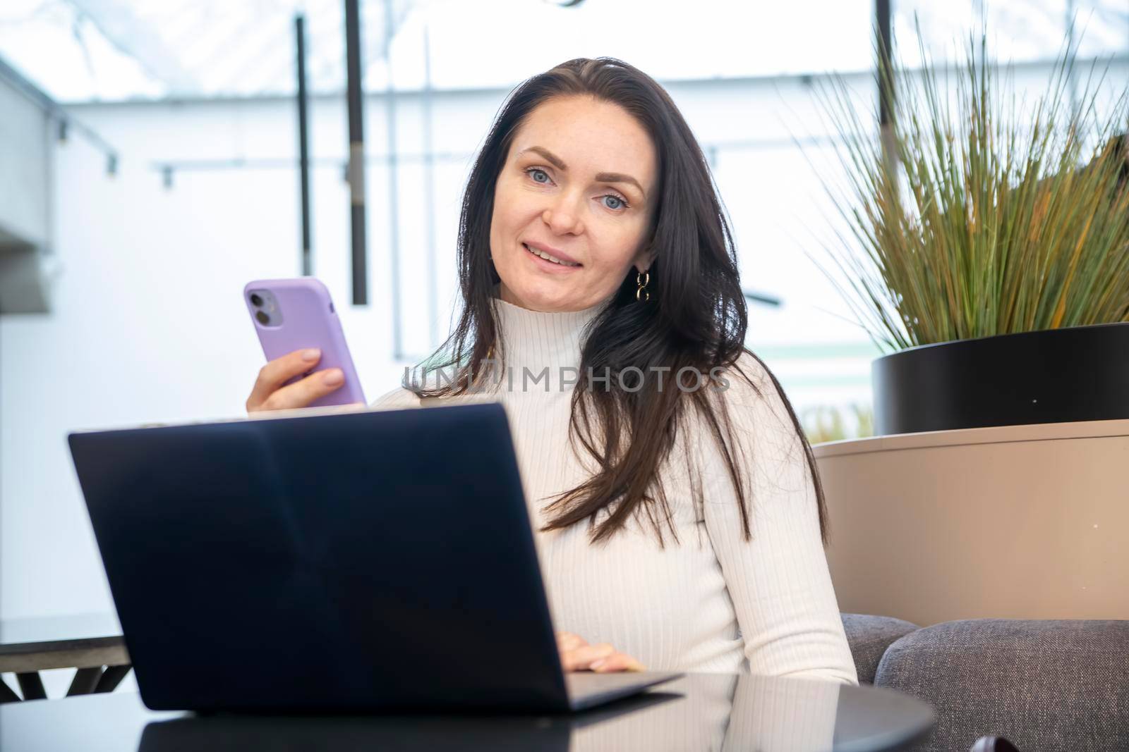 young woman works on laptop and smartphone in cafe.