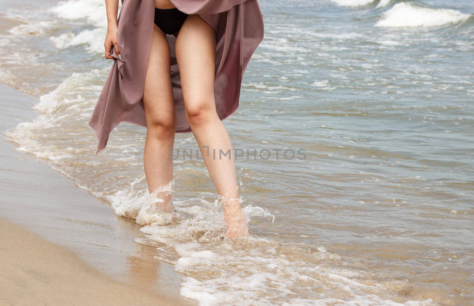 legs of a young woman standing on sand by sea by raddnatt