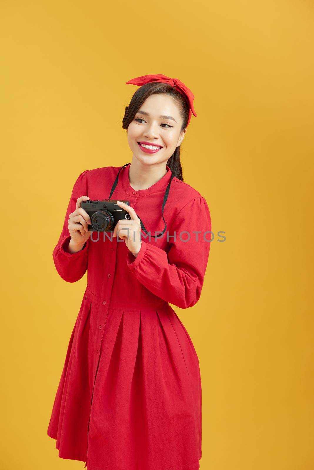Cheerful young Asian woman with digital camera ready enjoy travel over yellow isolated background.