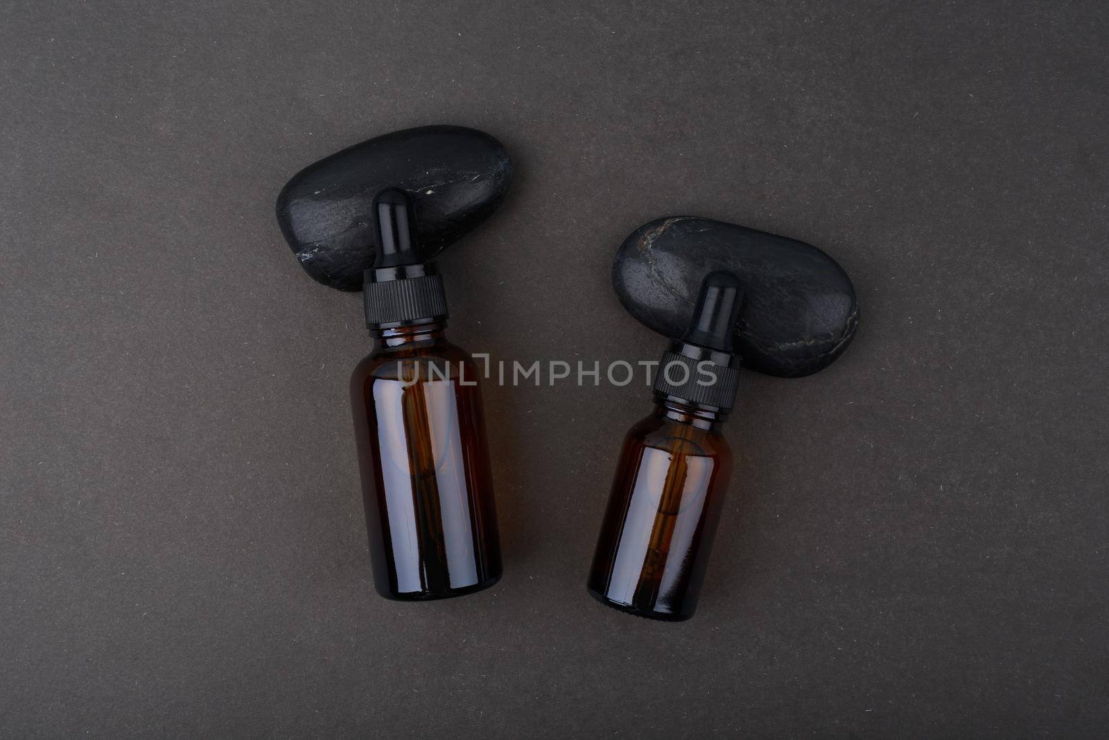 Flat lay in dark tones with two glass serum bottles with dropper on black background. Concept of skin care beauty products for man