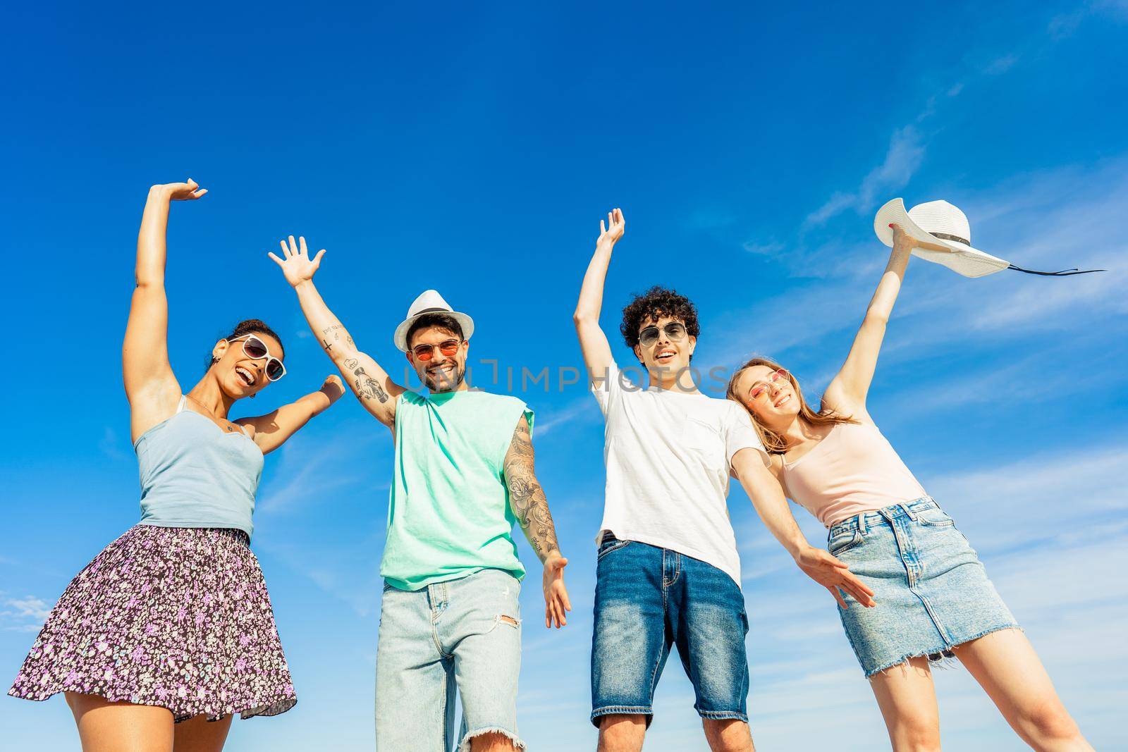 Young gen z happy multiracial friends group looking at camera for portrait in summer sea vacations. Bright vivid color photograph with blue sky. Diverse millennial people having fun at beach resort by robbyfontanesi