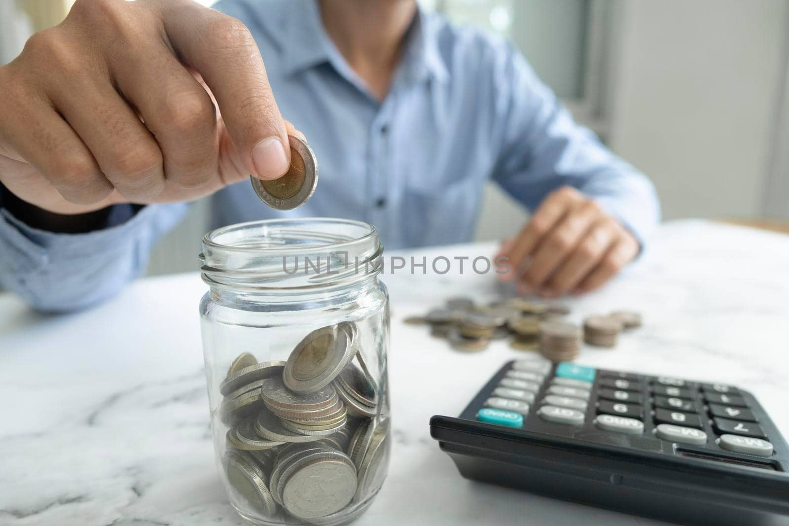 Businessman saving money concept. Hand holding coins putting in jug glass