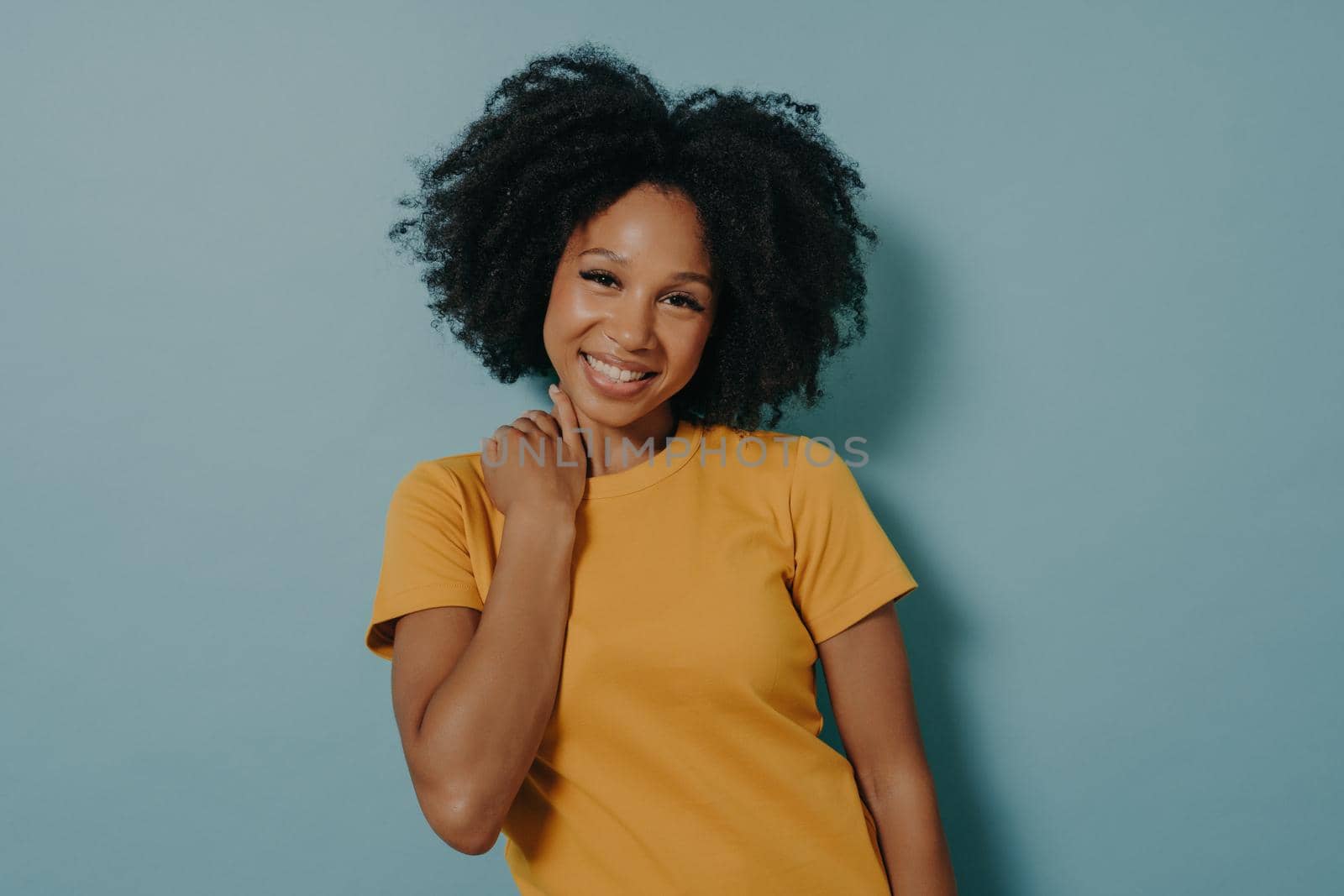 Portrait of beautiful cheerful girl smiling and looking at camera. Happy african woman in casual yellow tshirt. Stylish woman with one arm over shoulder posing in studio background with copy space