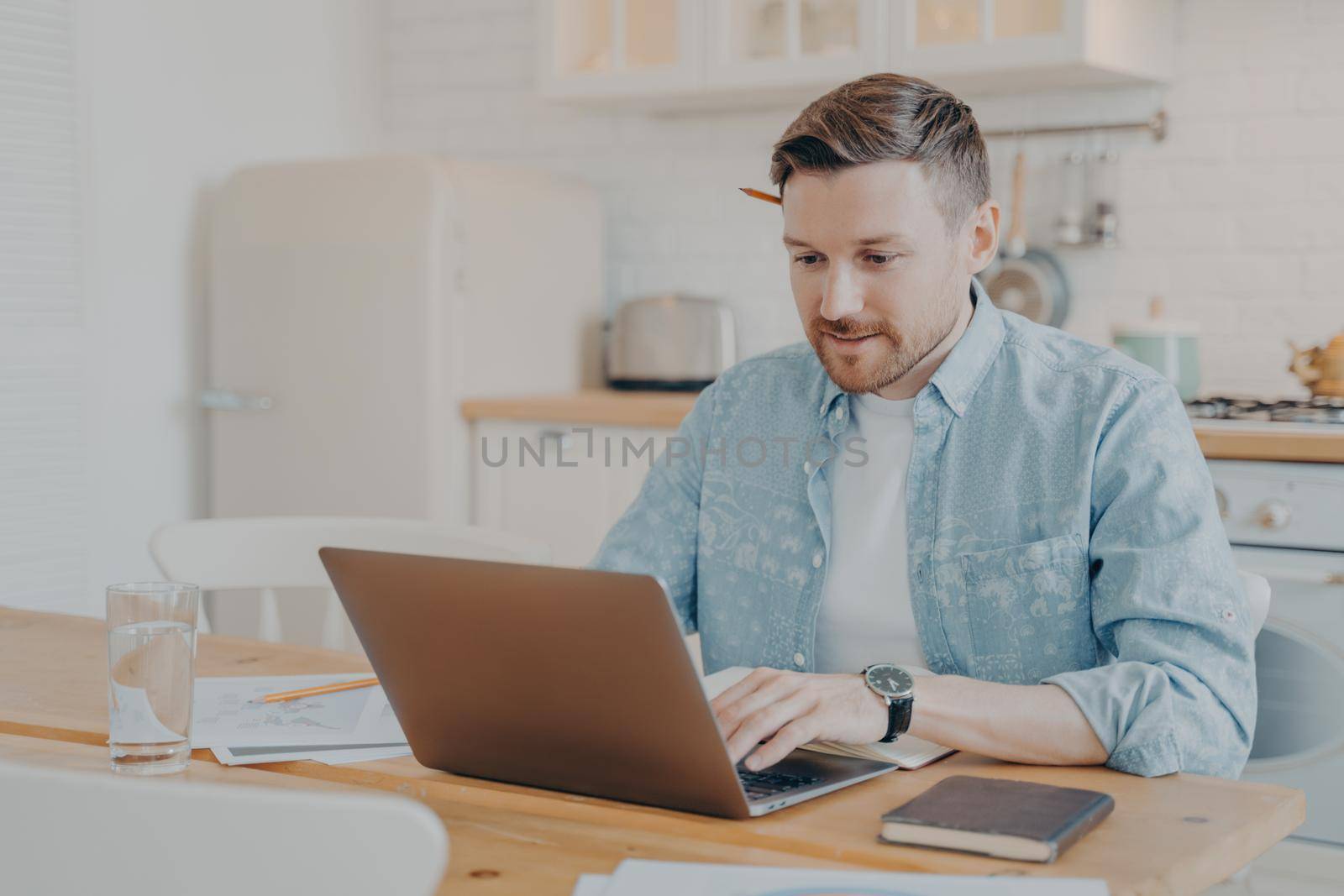 Focused young man freelancer using laptop while sitting at kitchen table by vkstock