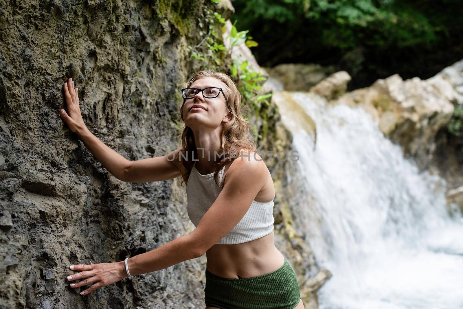 Summer travel. Young sexy woman in swimsuit enjoing the waterfall. Woman standing in front of waterfall and smiling