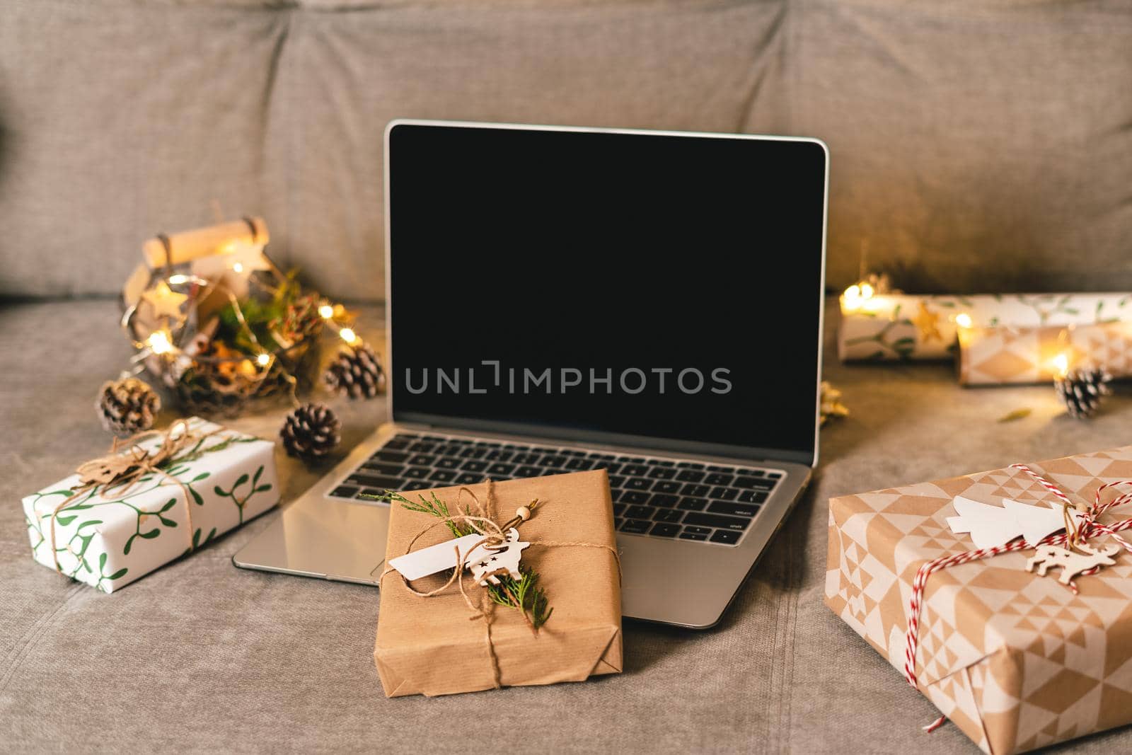Online shopping at Christmas holidays. Gifts, and mock up screen laptop on couch with natural eco presents and decor. Merry Christmas. Wrapping present boxes