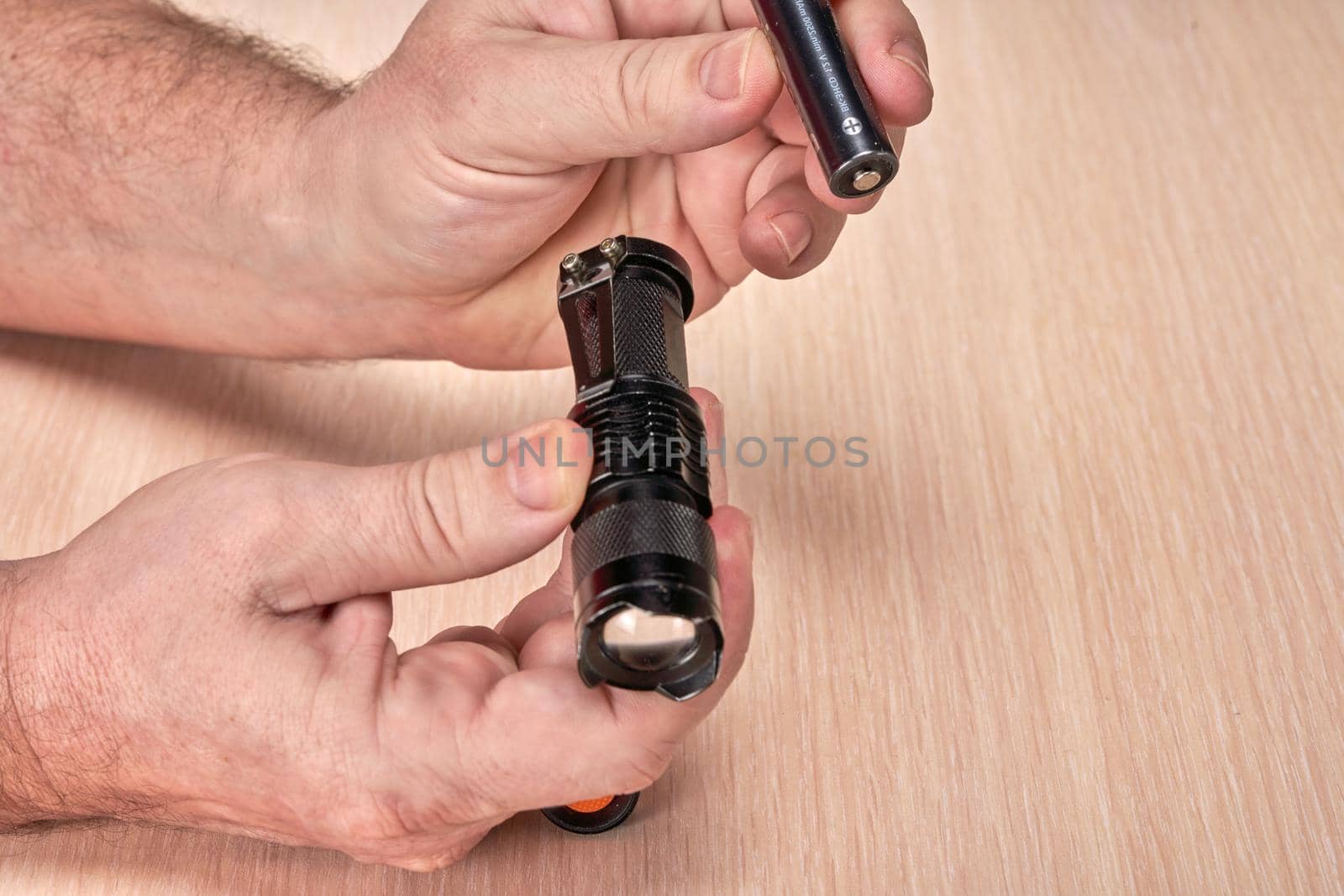 Hands hold a small black flashlight and replace the battery in it. Close up