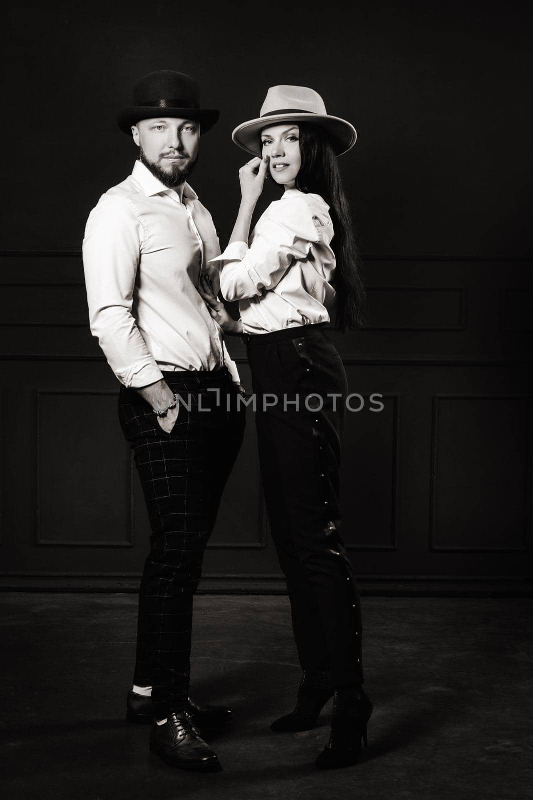 A man and a woman in white shirts and hats on a black background.A couple in love poses in the interior of the studio. black and white photo by Lobachad