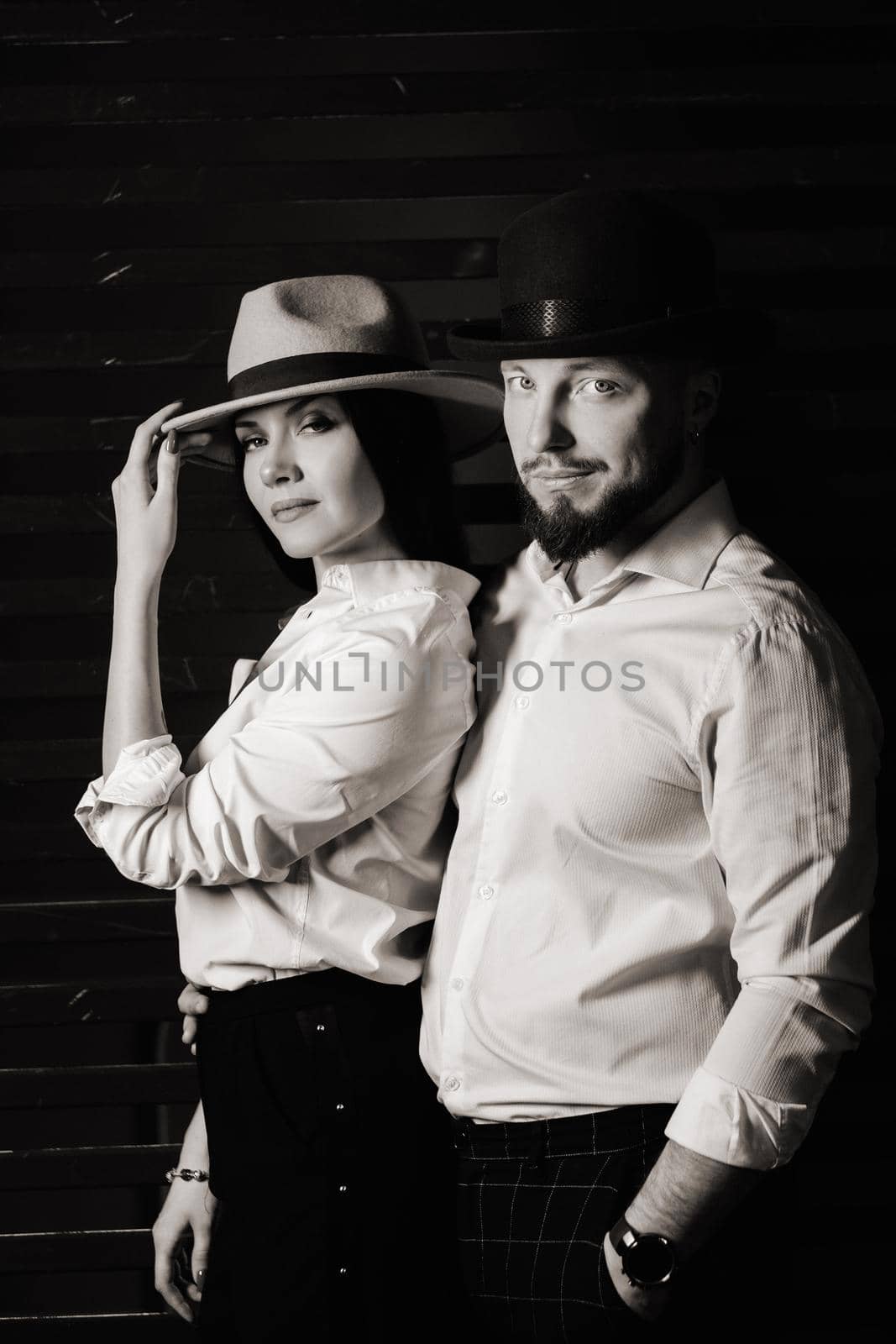 A man and a woman in white shirts and hats on a black background.A couple in love poses in the interior of the studio. black and white photo by Lobachad