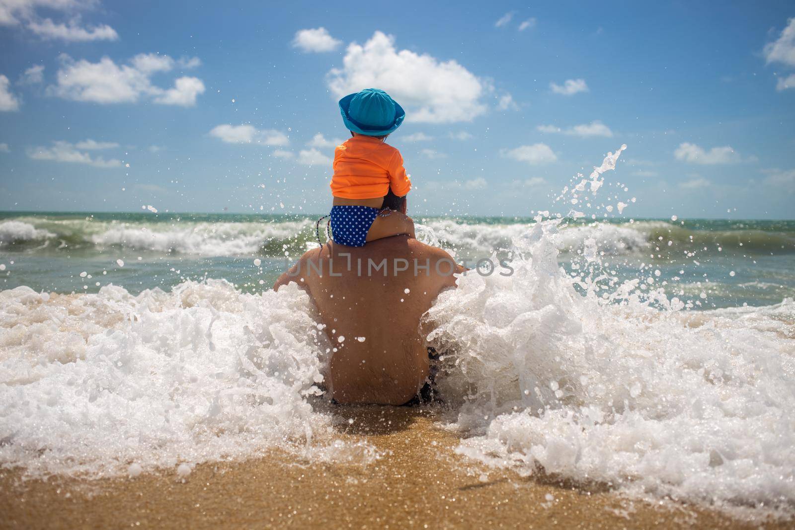 dad with a baby on his shoulders playing in the spray of sea foam. happy childhood concept