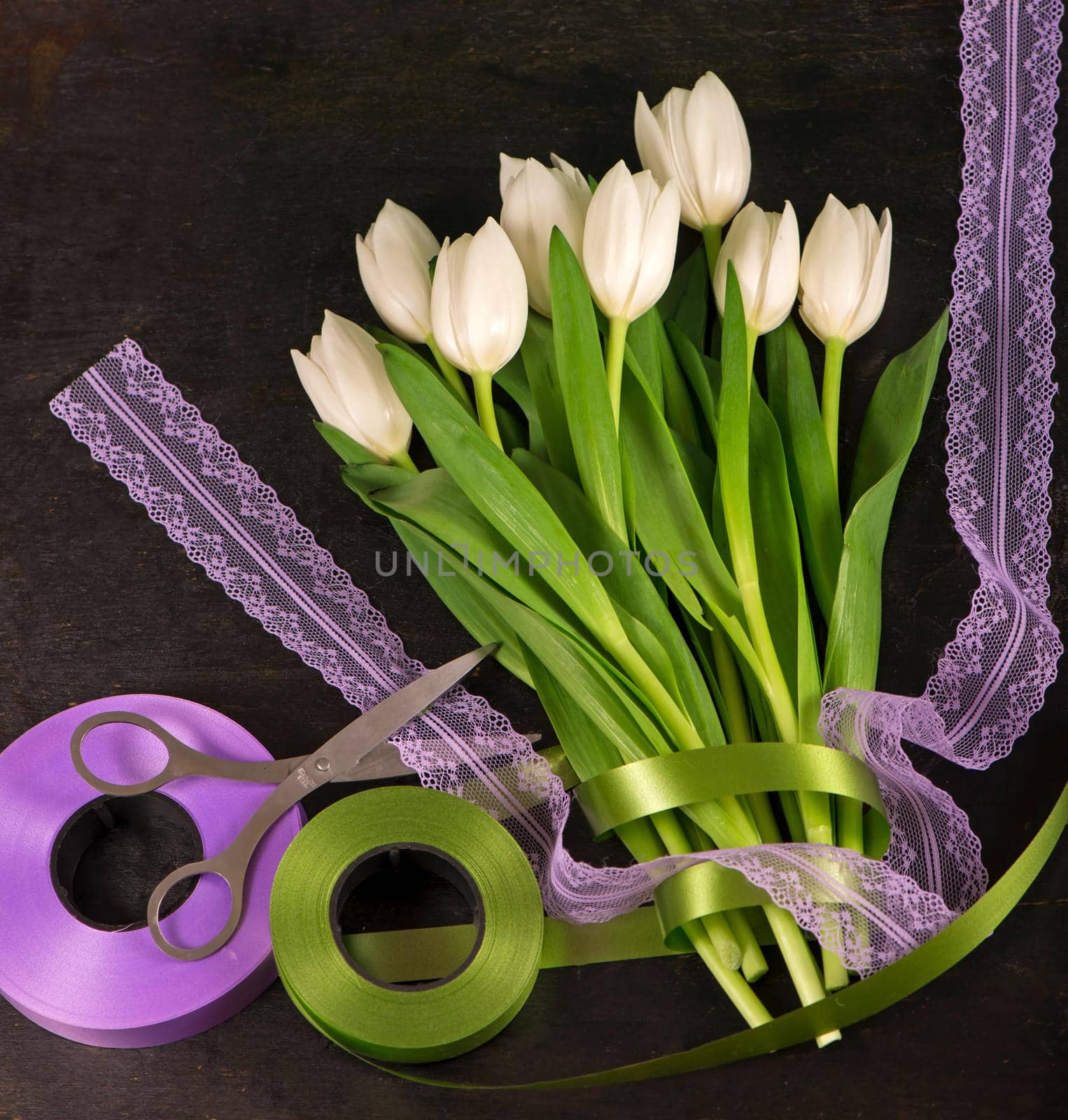 top view of beautiful tulips bouquet in wrapping paper, ribbons and old scissors on table