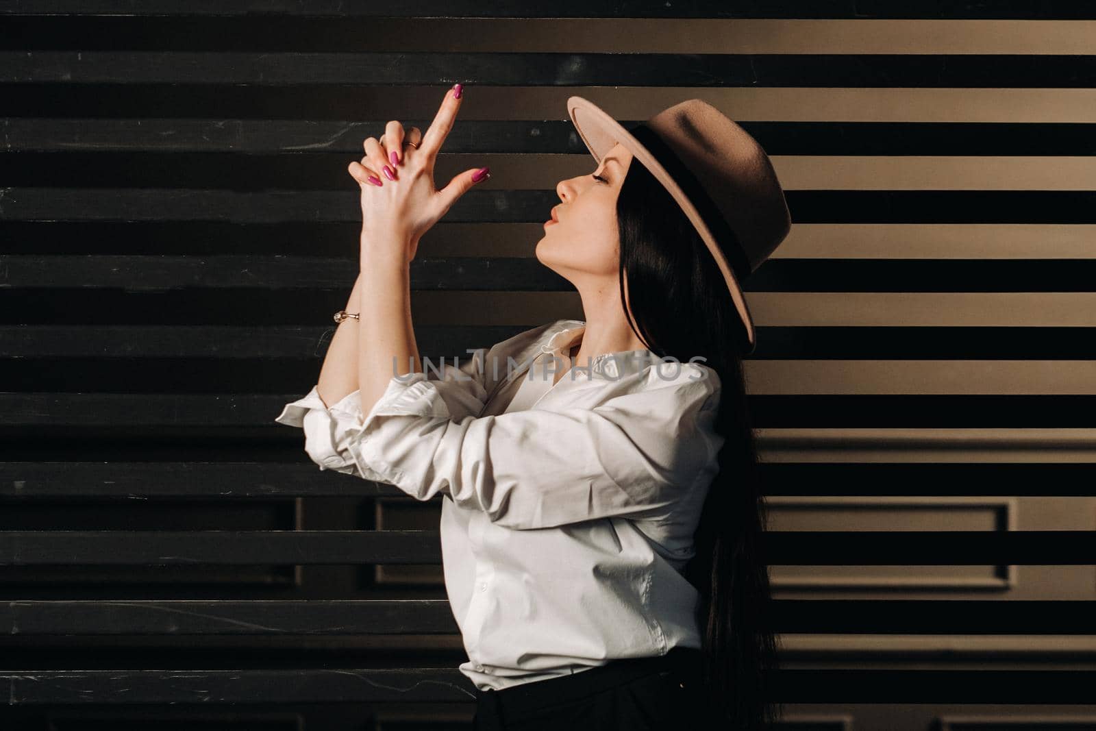 Elegant brunette girl in a white shirt and beige hat on a dark background.