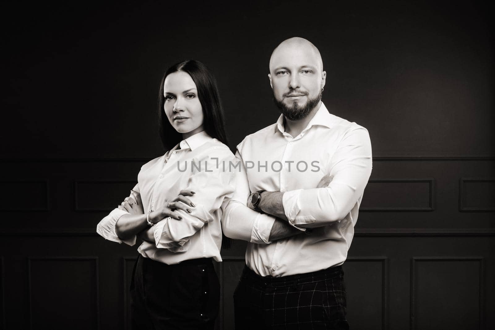 A man and a woman in white shirts on a black background.A couple in love in the studio interior.Black and white photo by Lobachad