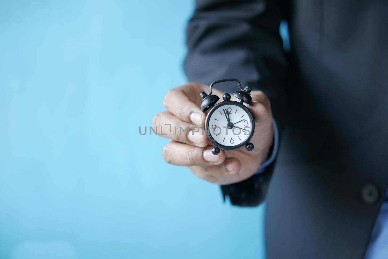 hand holding alarm clock against blue background .