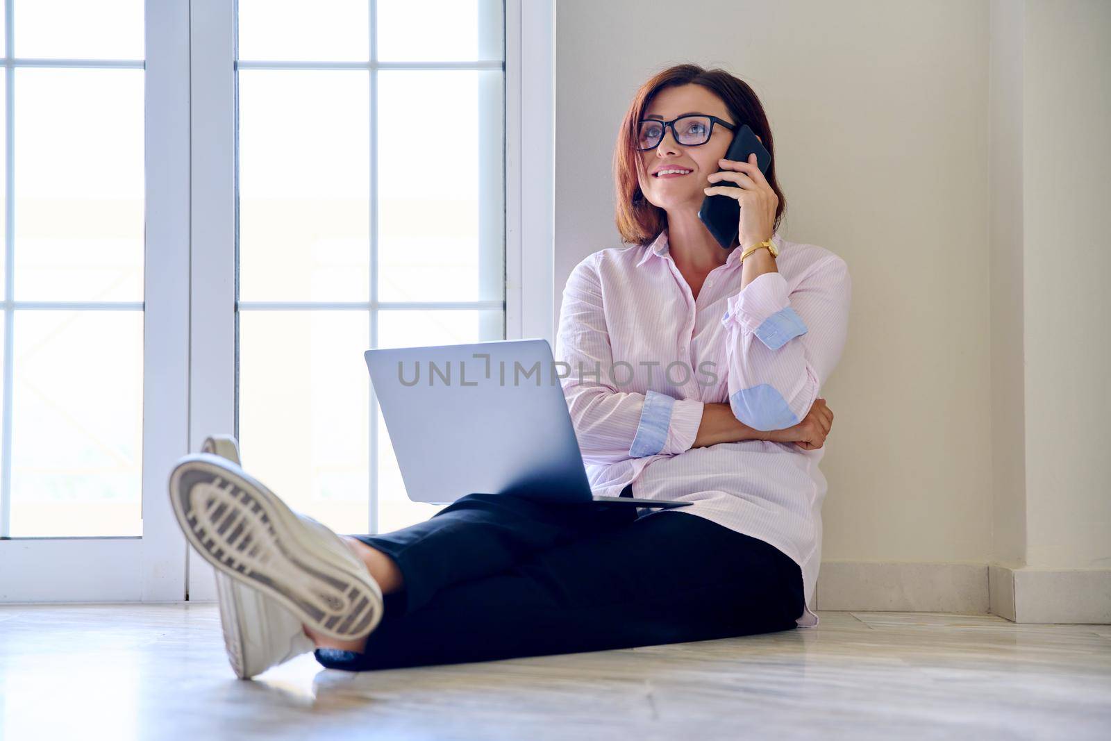 Business woman sitting on floor with laptop talking on smartphone, home office. Female psychologist counselor teacher mentor therapist analyst working online. Technology in business education medicine