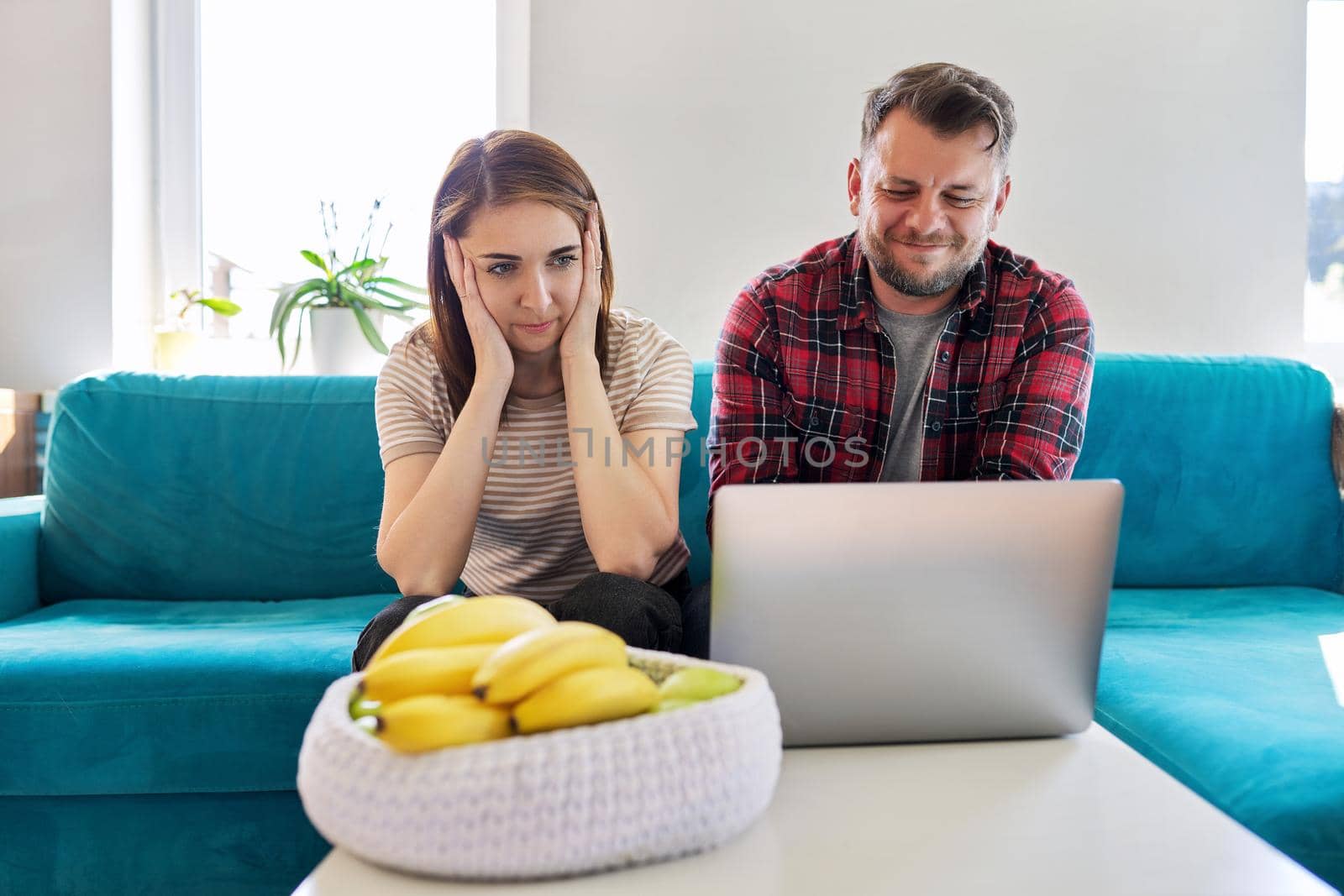 Serious middle aged couple looking at laptop screen at home in living room. Concentrated husband and wife listening looking into laptop, online information. Family, technology, lifestyle, 40s people