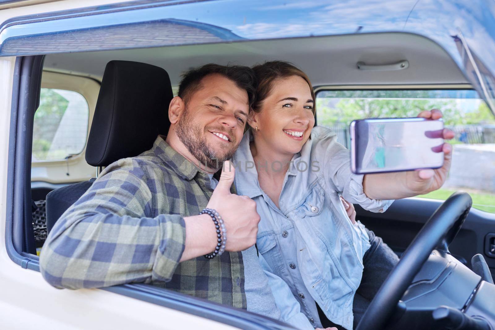 Happy married couple taking selfie photo on smartphone, husband and wife sitting in car.