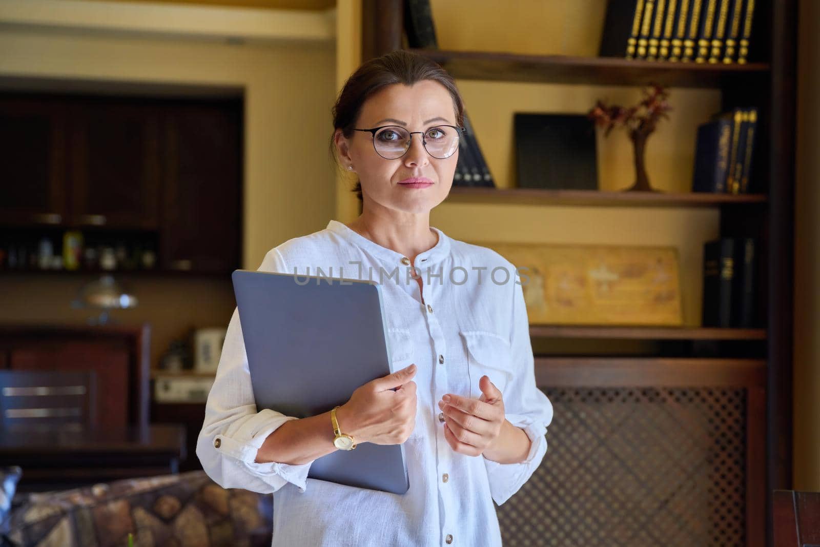 Portrait of a mature business woman in glasses with a laptop in her hands by VH-studio