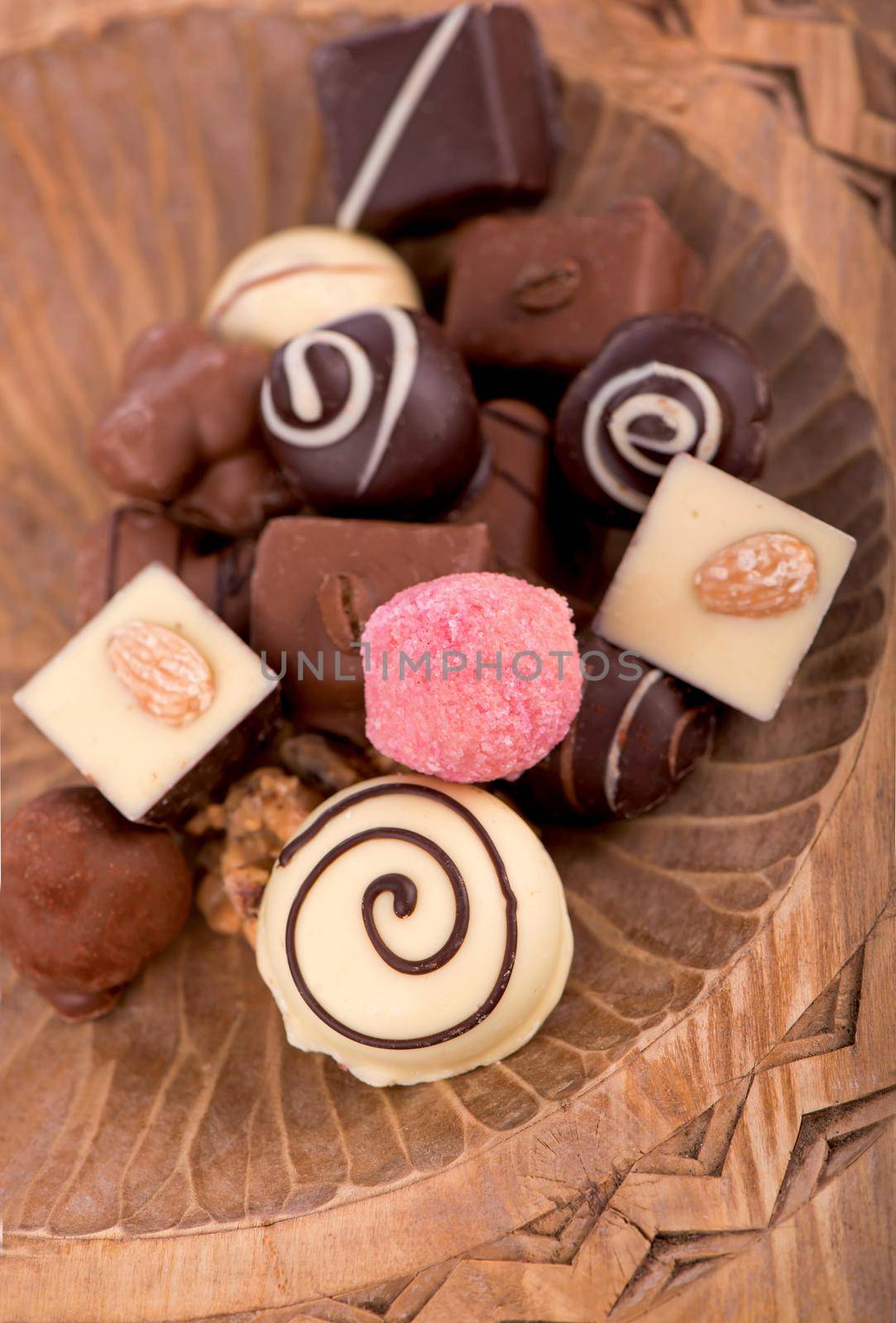 Broken bars of milk chocolate with nuts and sublimated berries and chocolate candies on rustic wooden background, with blank space for text top view, flat lay