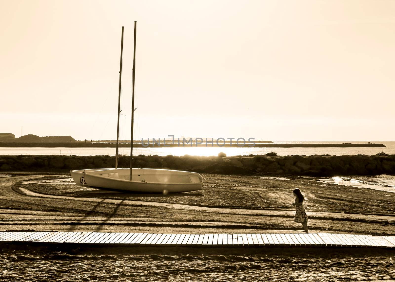 Santa Pola, Alicante, Spain- October 19, 2021: Beautiful sailboats on the shore and child running on Levante beach in Santa Pola, Alicante, Spain