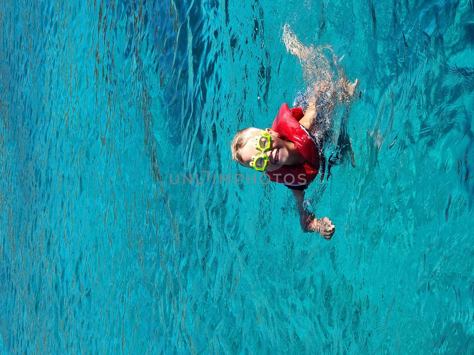 A child in swimming goggles and jelly bathes in the sea. Blue clear water.