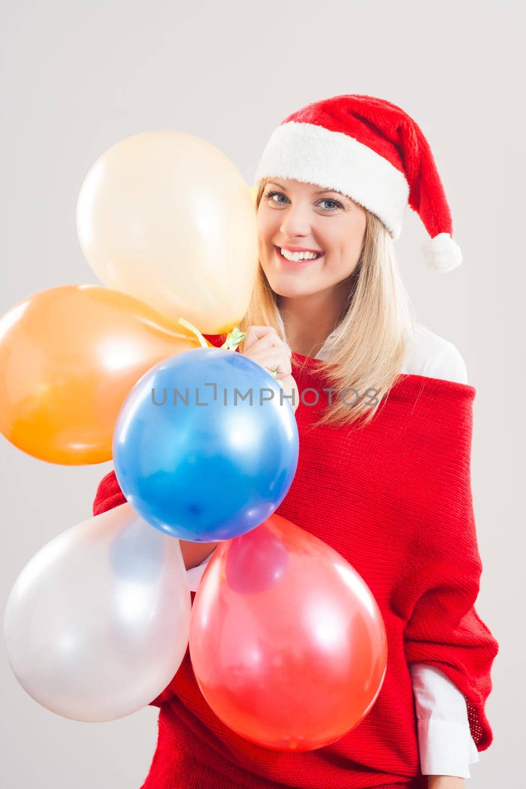 Beautiful young woman with Santa hat holding bunch of balloons.